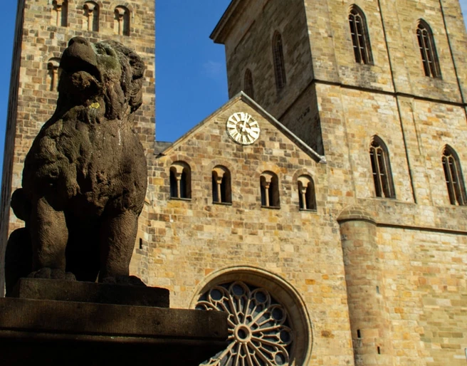 Altstadt-Highlights (Hauptbild).jpg Steinerne Skulptur eines Löwen vor einer historischen Kirche mit zwei Türmen und einer großen Uhr.Stone sculpture of a lion in front of a historic church with two towers and a large clock.Stenen beeld van een leeuw voor een historische kerk met twee torens en een grote klok.