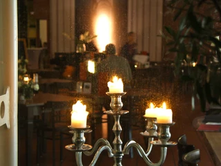 IMG_2946.JPG Kerzenständer mit brennenden Kerzen steht in einem dimm beleuchteten Raum mit verschwommenen Personen.Candlestick with burning candles stands in a dimly lit room with blurred people.