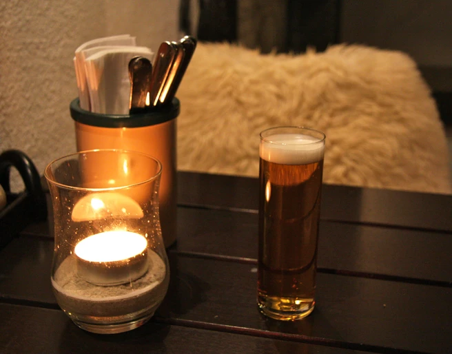 IMG_3073.JPG Kerze und Bierglas auf Holztisch neben Besteckhalter, warmes und gemütliches Ambiente.Candle and beer glass on wooden table next to cutlery holder, warm and cozy ambience.