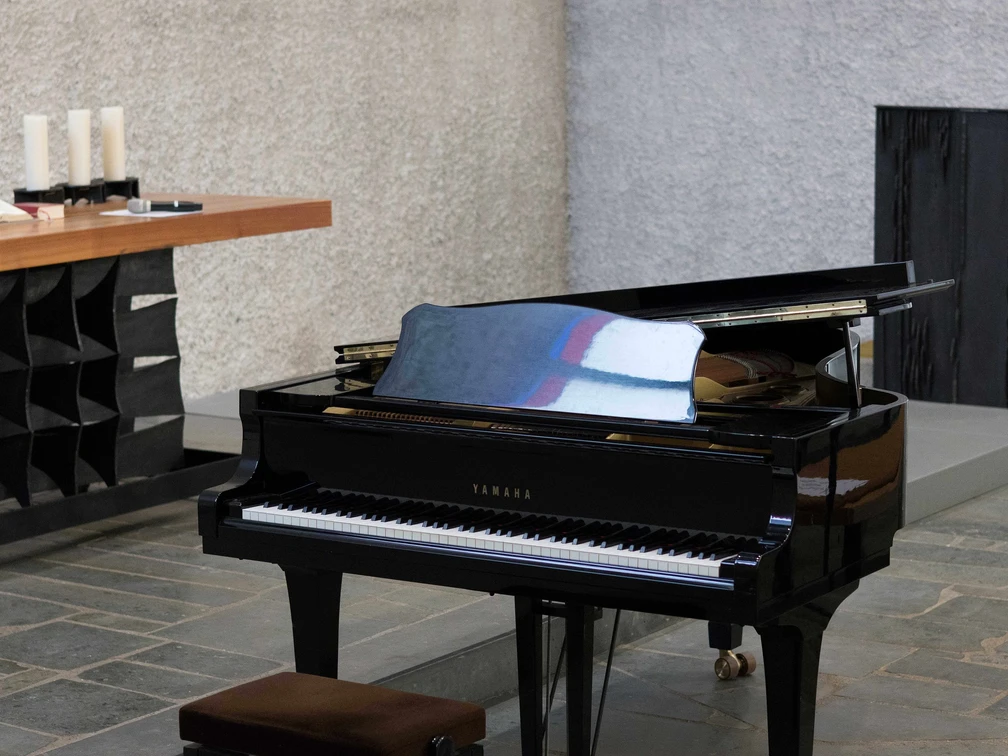 Liederabend Ein glänzender schwarzer Flügel steht in einem modernen Raum auf Steinboden, teilweise geöffnet.A shiny black grand piano stands in a modern room on a stone floor, partially open.