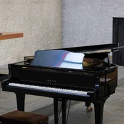 Liederabend Ein glänzender schwarzer Flügel steht in einem modernen Raum auf Steinboden, teilweise geöffnet.A shiny black grand piano stands in a modern room on a stone floor, partially open.