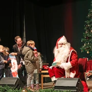 Schkeuditzer Weihnachtsmarkt - Weihnachten in der Region Leipzig  Der Weihnachtsmann sitzt neben einem geschmückten Baum und übergibt den Kindern Geschenke.
