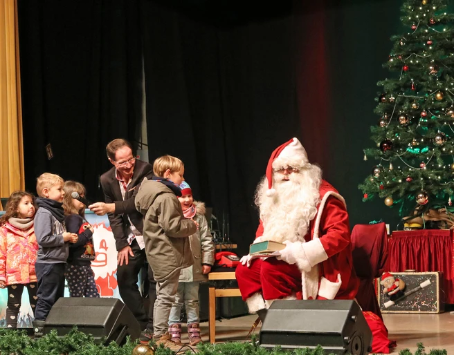 Schkeuditzer Weihnachtsmarkt - Weihnachten in der Region Leipzig  Der Weihnachtsmann sitzt neben einem geschmückten Baum und übergibt den Kindern Geschenke.