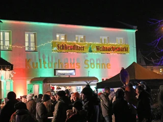 Kulturhaus Schkeuditzer Weihnachtsmarkt -Weihnachten in der Region Leipzig  Vor dem beleuchteten Kulturhaus auf dem Schkeuditzer Weihnachtsmarkt tummeln sich zahlreiche Besucher.