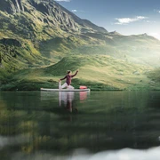 SUP Yoga auf dem Bettmersee Frau übt SUP Yoga Bettmersee im Sommer auf einem ruhigen Bergsee umgeben von grünen Hängen und alpiner Landschaft