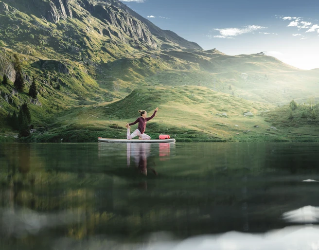 SUP Yoga auf dem Bettmersee Frau übt SUP Yoga Bettmersee im Sommer auf einem ruhigen Bergsee umgeben von grünen Hängen und alpiner Landschaft