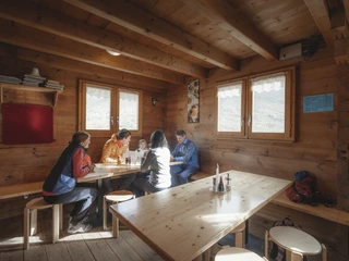 Gemütliche Pause in der Berghütte Teilnehmer der 2-Tage-Gletschertour Aletschgletscher sitzen in rustikaler Hütte beisammen und genießen eine Rast im Wallis