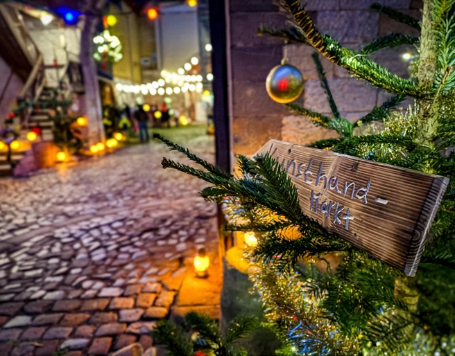 Adventsmarkt_Packhof_2024-1(1).jpg Einzigartig illuminierter Adventsmarkt mit Weg aus Kopfsteinpflaster, festliche Dekoration durch Tannenzweige und Lichterketten.