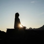 Yoga-Silhouette im Abendlicht Frau meditiert im Lotussitz auf einem Felsen beim Sonnenuntergang Yoga Aletsch Arena mit Blick auf die Berge