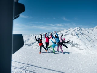 Gruppenfoto Skiline mit Alpenpanorama Gruppe springt in die Luft vor verschneiten Gipfeln beim Fotopoint während der Glacier Challenge Skiline Aletsch Arena