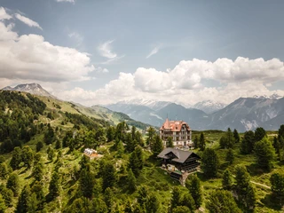 Luftaufnahme Villa Cassel inmitten der Berge Kräuterwanderung Aletsch Arena mit Panorama auf die Villa Cassel, eingebettet in die Bergwelt und den AletschwaldAletsch Arena herb hike with panoramic views of Villa Cassel, nestled in the mountains and the Aletsch ForestRandonnée sur le thème des herbes aromatiques dans l'Aletsch Arena avec panorama sur la Villa Cassel, nichée dans le paysage montagneux et la forêt d'Aletsch