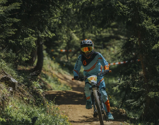 Kind im Bike-Rennen auf dem Flowtrail Kinderbikekurs Riederalp mit jungem Biker im Schutzanzug auf dem Flowtrail der Aletsch Arena