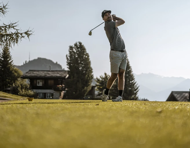Dynamischer Golfschwung vor Alpenpanorama Golf Schnupperkurs Aletsch Arena mit Spieler nach dem Abschlag auf dem Golfplatz Riederalp vor Bergkulisse