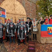 Aper_Markt.jpg Traditionell gekleidete Männer posieren in Ritterkostümen, umgeben von alten Backsteinmauern.