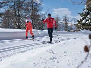 Cours de ski de fond sur la piste tracée de Riederalp Langlauf Schnupperkurs Riederalp mit zwei Teilnehmern auf gespurter Loipe vor verschneiter AlpenkulisseCross-country skiing taster course Riederalp with two participants on a groomed trail against a snowy Alpine backdropCours d'initiation au ski de fond à Riederalp avec deux participants sur une piste tracée devant un décor alpin enneigé