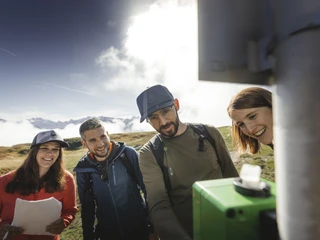 Team spirit at Foxtrail Desoria Foxtrail Desoria Aletsch Arena mit vier Teilnehmern, die gemeinsam eine Aufgabe an einer grünen Box lösenFoxtrail Desoria Aletsch Arena with four participants working together to solve a task at a green boxFoxtrail Desoria Aletsch Arena avec quatre participants qui résolvent ensemble une tâche sur une boîte verte