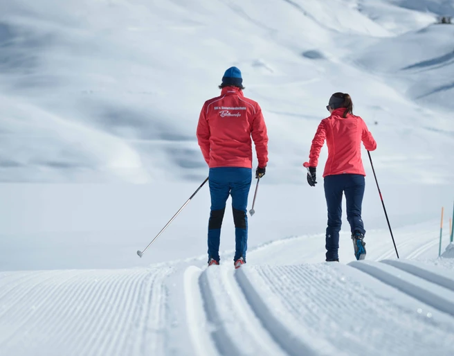 Gemeinsam auf der Loipe unterwegs Langlauf Schnupperkurs Bettmeralp in der Aletsch Arena mit zwei Teilnehmern nebeneinander auf verschneiter Winterloipe