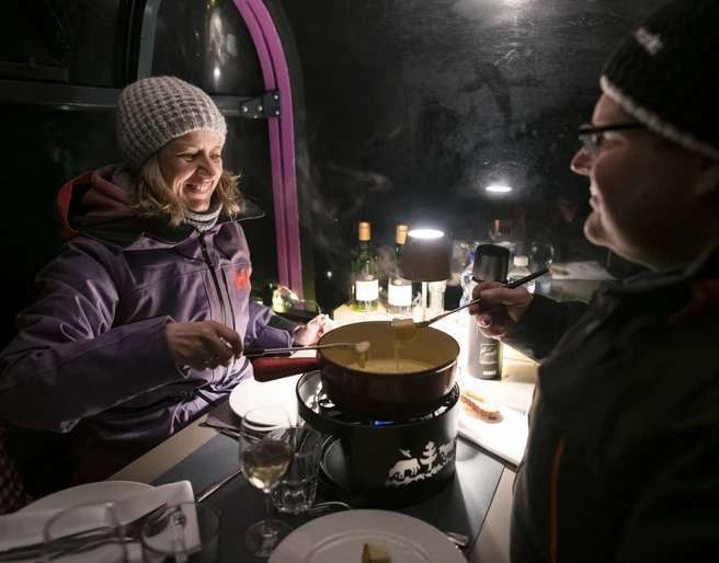 Genussvolles Fondueerlebnis im Winter Fonduegondel Bettmerhorn mit Paar beim Käsefondue in stimmungsvoller Gondel am Abend in der verschneiten Aletsch Arena