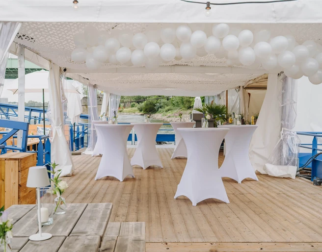 IMG_4664.JPG Weiße Stehtische und runde Ballons unter Pavillon auf Holzdeck mit Seeblick.White bar tables and round balloons under a pavilion on a wooden deck with a view of the lake.