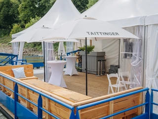 IMG_4611.JPG Eleganter, überdachter Sitzbereich auf einem Holzdeck mit Tischen und weißen Sonnenschirmen.Elegant, covered seating area on a wooden deck with tables and white parasols.