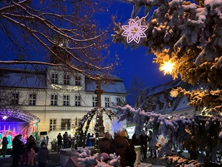 Weihnachtsmarkt Bad Düben - Weihnachten in der Region Leipzig  Bunte Lichter tauchen den Weihnachtsmarkt vor dem Rathaus in ein zauberhaftes Licht, während ein festlich geschmückter Weihnachtsbaum mit funkelnden Sternen und Schneedecke die Szenerie erhellt.