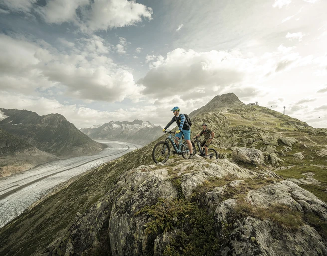 Mountainbiken mit Gletscherblick Aletsch Bikepass mit Bikern auf dem Trail oberhalb des Grossen Aletschgletschers mit weiter Aussicht über die Aletsch Arena