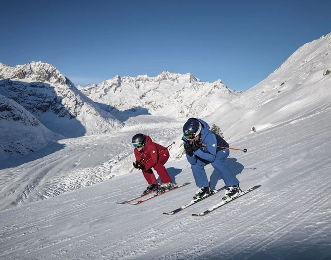 Skifahren mit Blick auf den Aletschgletscher Skipass Aletsch Arena mit zwei Skifahrern auf perfekt präparierter Piste oberhalb des Aletschgletschers bei strahlendem Winterwetter