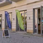 Aktivzentrum Touristinformation Bad Schandau Bunte Werbefahnen vor einem Eingang mit Tafel auf Gehweg.