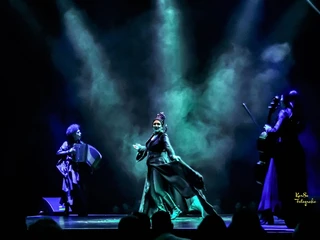 Cirque Bouffon - Célébration  Dunkle Bühne mit dramatischer Beleuchtung und vier Musiker*innen in schwarzen Kostümen.Dark stage with dramatic lighting and four musicians in black costumes.