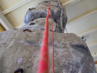 Indoor Hochseilgarten Kanuaktivtours Kletterwand aus Kunststoff mit roter Kletterseilführung in Innenraum.