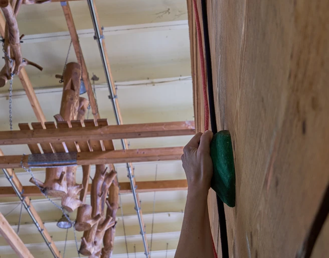Indoor Hochseilgarten Kanuaktivtours Hand hält grünen Griff beim Klettern an einer Holzwand im Hintergrund Klettergeräte an der Decke.