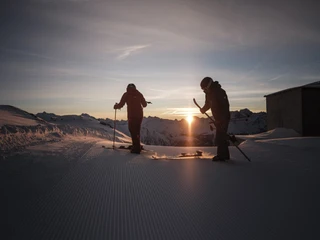 Skistart im ersten Licht des Tages First Track Bettmerhorn mit Skifahrern im Sonnenaufgang auf frisch präparierter Skipiste der Aletsch Arena