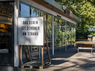 Blackfoot Beach Holzterrasse mit Strandbar und Tischtennisplatte, umgeben von Bäumen und Sonnenschein.Wooden terrace with beach bar and table tennis table, surrounded by trees and sunshine.
