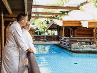 Außenbereich der Kurhessen Therme Zwei Personen stehen in Bademänteln im Außenbereich der Kurhessen Therme. Ein Sauna ist sichtbar sowie das Außenbecken.Two people stand in bathrobes in the outdoor area of the Kurhessen Therme. A sauna and the outdoor pool are visible.