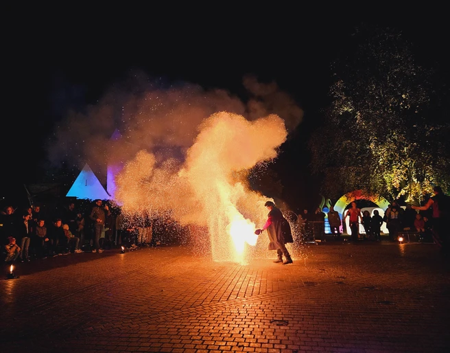 Feuershow der Rasteder Lichternacht.jpg Feuershow in der Nacht mit Funkenregen, umgeben von Zuschauern und bunt beleuchteten Zelten.