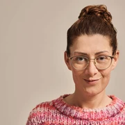 Jana Crämer Ein aufschlussreiches Porträtfoto einer lächelnden Frau mit Brille und buntem Pullover.A revealing portrait photo of a smiling woman with glasses and a colorful sweater.