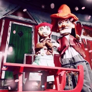 Zwei Puppen, Petersson und Findus, stehen vor einer rot-weißen Hütte im Schnee.