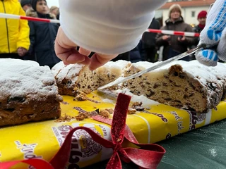 Oschatzer Weihnachtsmarkt - Weihnachten in der Region Leipzig Eine Hand schneidet einen großen Stollen auf einem Tisch, der mit Puderzucker bestreut ist.