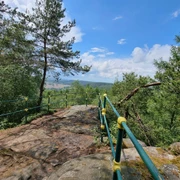 Hartenstein Aussichtspunkt mit grün-gelben Geländer, Bäumen und Blick auf eine Landschaft.