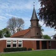 Kath. Kirche Augustfehn, Außenansicht von vorn, Foto Kath. Kirche.JPG Backsteinkirche mit kleinem Spitzturm und rotem Ziegeldach, umgeben von Rasen und Bäumen.