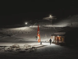 Stimmungsvolles Nachtskifahren beim Familienskilift Fieschertal Das Nachtskifahren Fieschertal zeigt die beleuchtete Talstation des Familienskilifts Blaetz mit Skifahrern und gemütlicher Hüttenatmosphäre in der Aletsch Arena