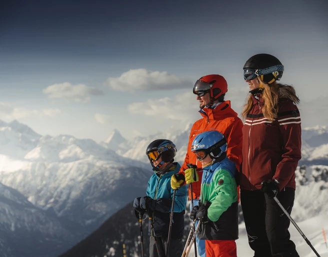 Familie geniesst Skitag mit Panorama in der Aletsch Arena Beim Familien Skipass Aletsch Arena geniesst eine Familie den Blick auf die verschneiten Walliser Alpen während einer Skitour bei sonnigem Wetter