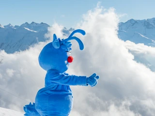 Gletschi Maskottchen begrüsst Familien in der Aletsch Arena Beim Familien Skipass Aletsch Arena begrüsst das blaue Maskottchen Gletschi lachend die Skifahrer vor verschneiter Alpenkulisse im Winter