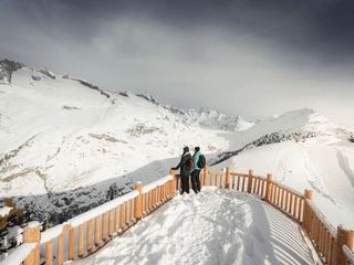 Panorama hivernal du View Point Hohfluh sur le glacier d'Aletsch Das View Point Package Aletsch zeigt zwei Winterwanderer auf dem Aussichtspunkt Hohfluh mit Blick über den verschneiten Grossen AletschgletscherThe View Point Package Aletsch shows two winter hikers at the Hohfluh vantage point with a view over the snow-covered Great Aletsch GlacierLe View Point Package Aletsch montre deux randonneurs hivernaux sur le point de vue de Hohfluh avec vue sur le Grand glacier d'Aletsch enneigé.