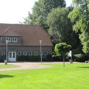 Bokler Schule.JPG Backsteingebäude mit rotem Dach, umgeben von grüner Wiese und Bäumen bei sonnigem Wetter.