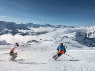 Un ski dynamique avec vue sur les Alpes valaisannes Beim Wahltages Skipass Aletsch Arena fahren zwei Skifahrer in eleganten Schwüngen über die breite Panoramapiste mit Blick auf die Walliser AlpenWith the optional Aletsch Arena ski pass, two skiers make elegant turns on the wide panoramic slope with views of the Valais AlpsAvec le forfait à choix Aletsch Arena, deux skieurs effectuent des virages élégants sur la large piste panoramique avec vue sur les Alpes valaisannes.