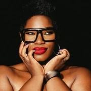 Porträt einer selbstbewussten Person mit markanter, schwarzer Brille und rotem Lippenstift.