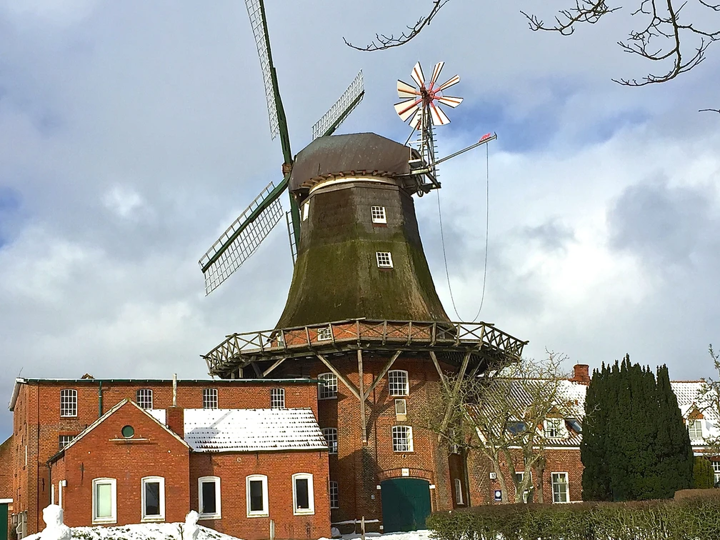 Mühle Pewsum im Winter Zu sehen ist die Mühle Pewsum im Winter, es liegt ein bisschen Schnee, im Vordergrund steht ein altes Fahrrad als Deko.
