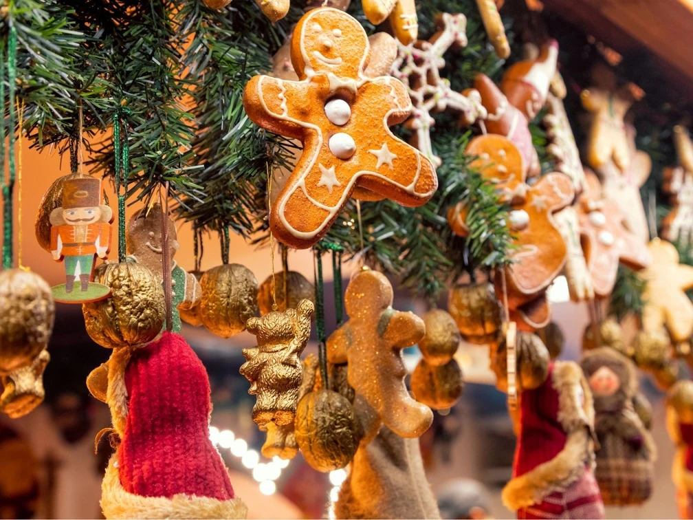 Destination Kalenderbilder(1).jpg Lebkuchen, Nussknacker und goldene Nüsse hängen an grünen Zweigen mit warmem Licht.