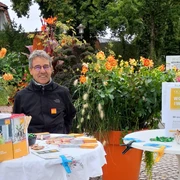 Reiner Dunker, Energieexperte Verbraucherzentrale Niedersachsen.jpg Ein Mann mit Infostand zur Energieberatung vor blühenden Pflanzen im Freien.